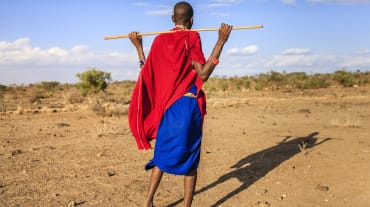 Persona Masai di spalle, con in mano un bastone di legno.