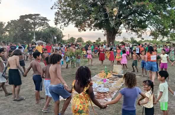 Decine di persone, tra donne, uomini, bambini e anziani, formano un cerchio attorno a un'offerta stesa a terra con alimenti, semi e altri prodotti della terra