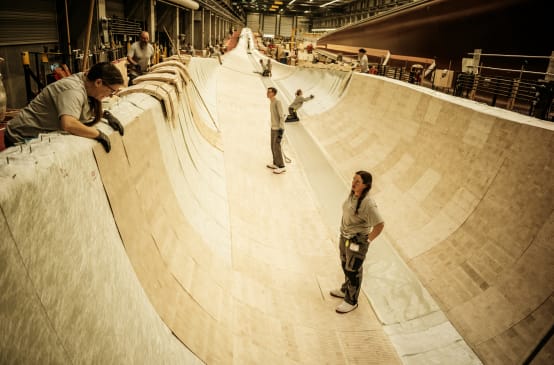 Diverse persone si trovano all'interno del rivestimento in legno di balsa per la costruzione della pala di un rotore.