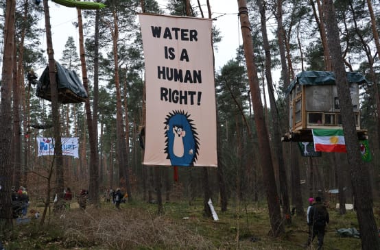 Striscione con la scritta in inglese "Water is a Human Right" (L'acqua è un diritto umano) appeso agli alberi dell'accampamento contro l'espansione della megafabbrica di Tesla a Grünheide.