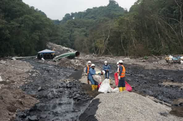 Un gruppo di lavoratori petroliferi lavora tra due fiumi neri di petrolio che scendono da una montagna coperta di rocce nella foresta. Una sezione di tubo dell'oleodotto si vede sullo sfondo.