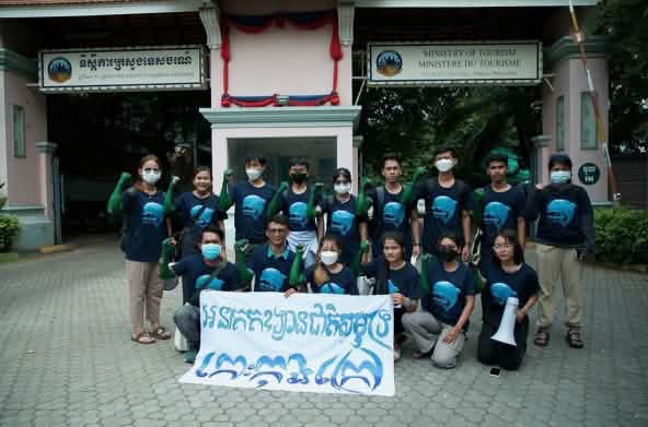 15 giovani sono in piedi e in ginocchio davanti all'edificio del Ministero del Turismo e tengono uno striscione verso la macchina fotografica. Lo striscione recita: "L'isola di Koh Kong deve diventare un parco nazionale marino".