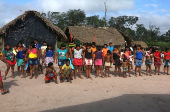 Gli indigeni Kaapor in piedi, in fila, davanti a due capanne nella foresta