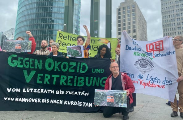 Un gruppo di persone protesta con grandi striscioni colorati davanti a tre edifici per uffici