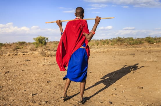 Persona Masai di spalle, con in mano un bastone di legno.