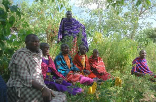 Un gruppo di uomini Maasai, vestiti con abiti dai colori vivaci, seduti sull’erba