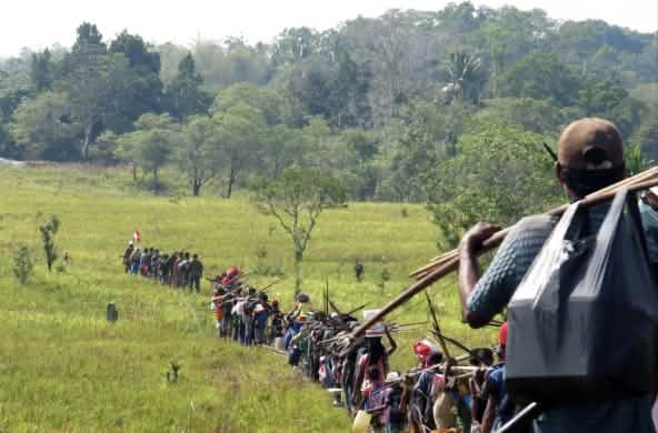 Fila indiana di indigeni che attraversano una savana per andare a caccia