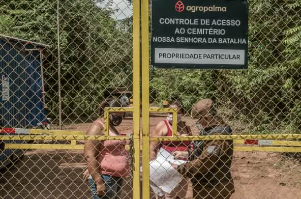 Due donne controllate da una guardia dietro un cancello sbarrato - Testo scritto sul cartello dell'azienda: Agropalma - Controllo dell'accesso al cimitero di Nossa Senhora da Batalha. PROPRIETÀ PRIVATA