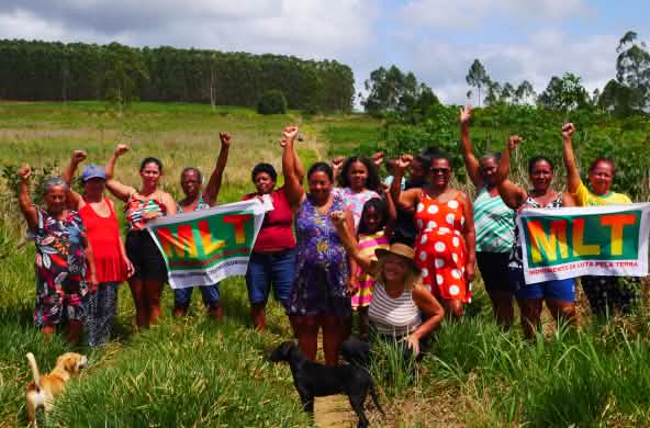 Un gruppo di 15 donne protesta con i pugni alzati e due striscioni con la scritta "MLT Movimento de Luta pela Terra".