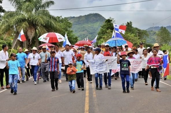 Dimostranti marciano con striscioni, bandiere nazionali e ombrelli lungo un'autostrada a Panama.