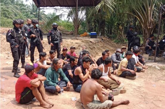 Indigeni Dayak arrestati siedono a terra con la polizia armata alle spalle.