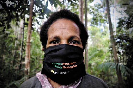 Donna papuana che indossa una maschera con la scritta "Proteggi la foresta - la foresta ci protegge".