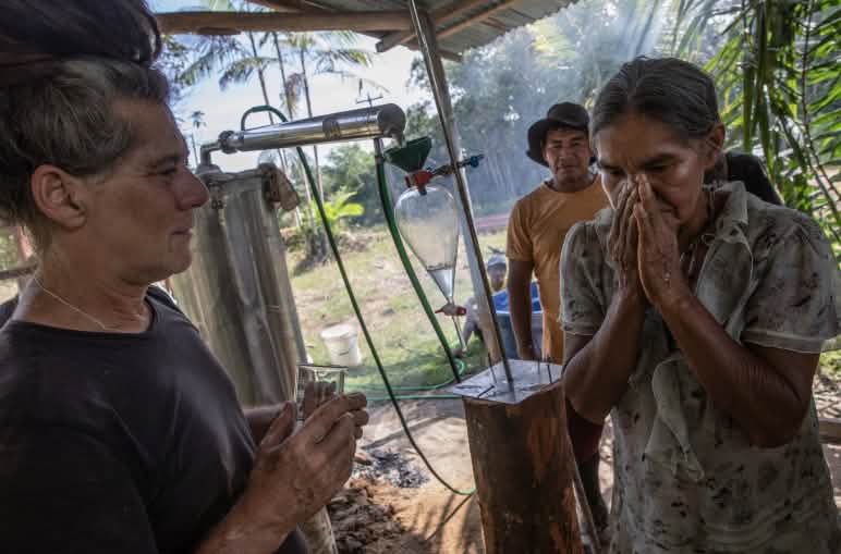 Una donna indigena, accanto a un distillatore a vapore, annusa gli oli essenziali che il formatore le ha versato sulla mano;