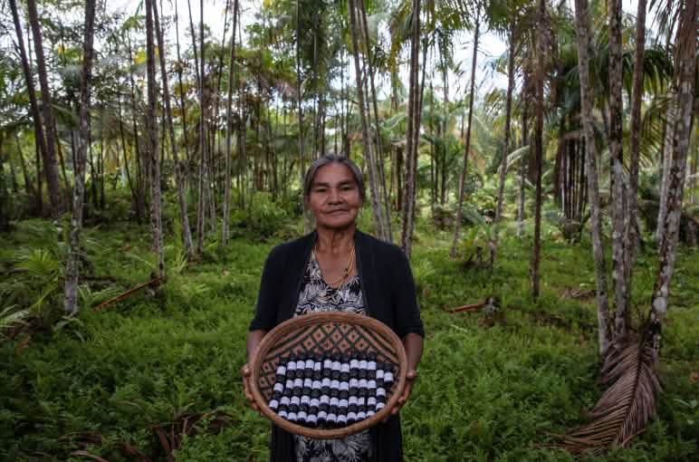 Una donna indigena nella foresta pluviale mostra una cesta piena di boccette di oli essenziali