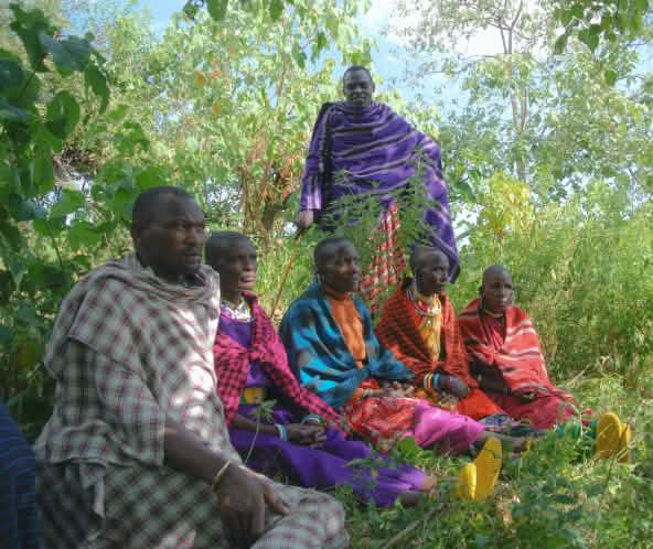 Un gruppo di uomini Maasai, vestiti con abiti dai colori vivaci, seduti sull’erba