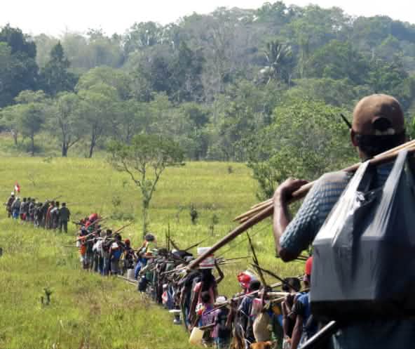 Fila indiana di indigeni che attraversano una savana per andare a caccia