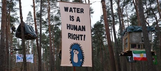 Striscione con la scritta in inglese "Water is a Human Right" (L'acqua è un diritto umano) appeso agli alberi dell'accampamento contro l'espansione della megafabbrica di Tesla a Grünheide.