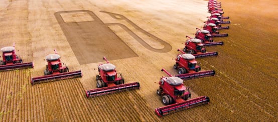 Fotomontaggio: Fotomontaggio: 15 mietitrebbie al lavoro in un campo di soia lasciano una scia a forma di pompa di benzina