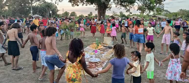 Decine di persone, tra donne, uomini, bambini e anziani, formano un cerchio attorno a un'offerta stesa a terra con alimenti, semi e altri prodotti della terra