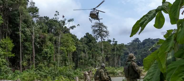 Due agenti armati dell'agenzia ambientale IBAMA, in tuta mimetica, sotto un elicottero durante un'operazione contro l'estrazione illegale di oro nella foresta amazzonica.