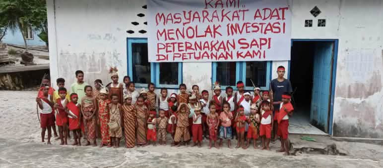 «Noi indigeni rifiutiamo che si investa nell'allevamento bovino sulle nostre terre ancestrali!» Gruppo di bambini davanti a una scuola su cui è appeso uno striscione con un messaggio in indonesiano