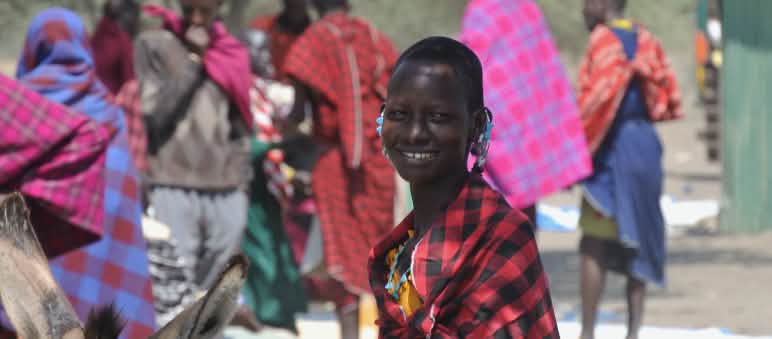 Donna Masai in un mercato vicino al cratere di Ngorongoro Donne e uomini Maasai in abiti colorati in un mercato, una donna guarda nell'obiettivo
