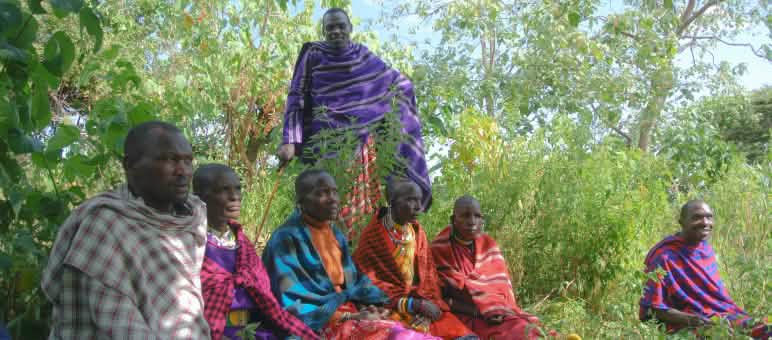 Un gruppo di uomini Maasai, vestiti con abiti dai colori vivaci, seduti sull’erba