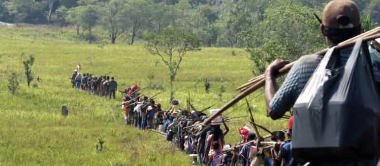 Fila indiana di indigeni che attraversano una savana per andare a caccia