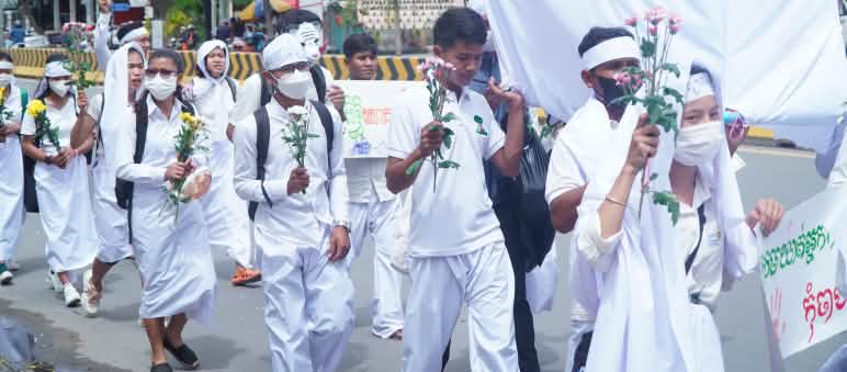 Giovani vestiti di bianco camminano per una strada con fiori in mano a Phnom Penh.