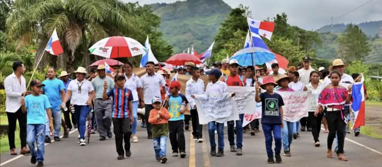 Dimostranti marciano con striscioni, bandiere nazionali e ombrelli lungo un'autostrada a Panama.