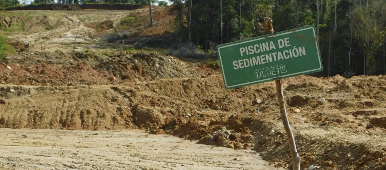 Paesaggio devastato dalla presenza di bacini di sedimentazione, sui quali è visibile un cartello con scritte in spagnolo e cinese.