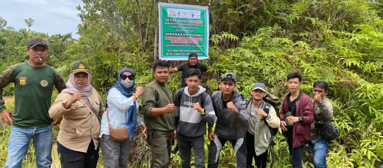 Un gruppo di persone davanti a un cartello di avvertimento che segnala pesanti sanzioni per qualsiasi attività nella foresta.