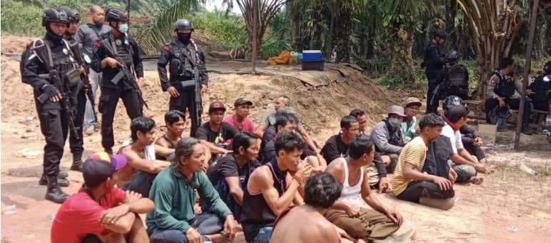 Indigeni Dayak arrestati siedono a terra con la polizia armata alle spalle.