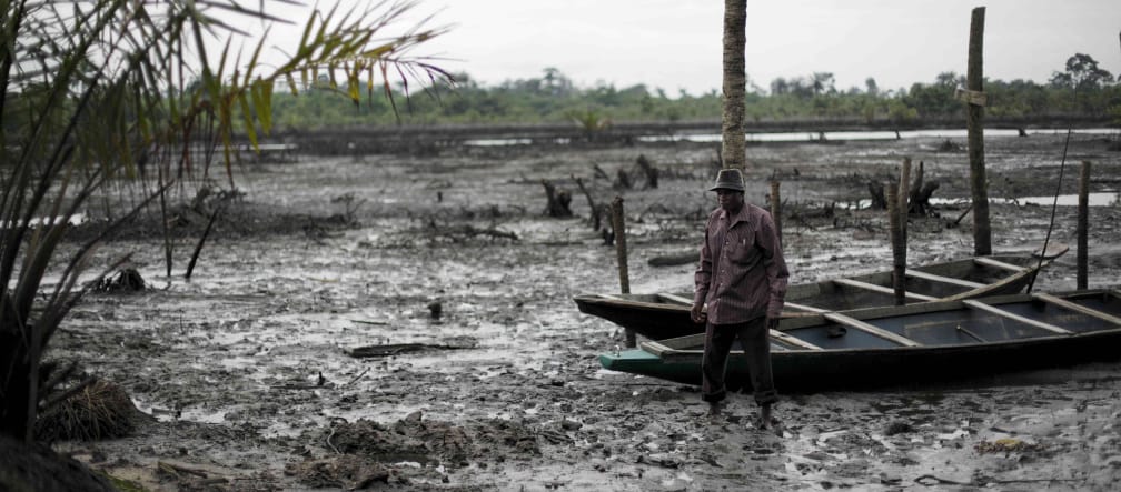 Un uomo si trova nel letto di un fiume inquinato dal petrolio nel Delta del Niger.