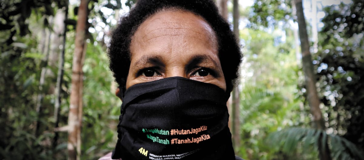 Donna papuana che indossa una maschera con la scritta "Proteggi la foresta - la foresta ci protegge".