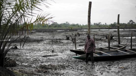 Un uomo si trova nel letto di un fiume inquinato dal petrolio nel Delta del Niger.
