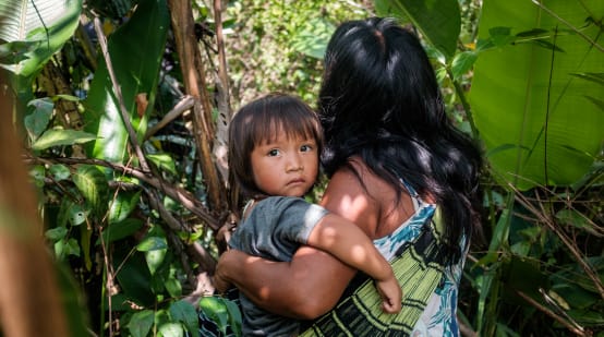 Donna indigena Ka'apor nella vegetazione della foresta amazzonica con il suo bambino in braccio.