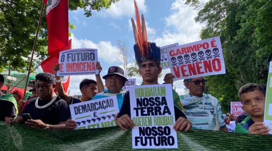 Indigeni che marciano in fila reggendo cartelli con slogan come: “La nostra terra è il nostro futuro”