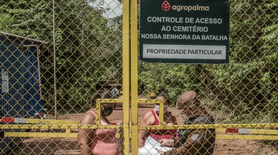 Due donne controllate da una guardia dietro un cancello sbarrato - Testo scritto sul cartello dell'azienda: Agropalma - Controllo dell'accesso al cimitero di Nossa Senhora da Batalha. PROPRIETÀ PRIVATA