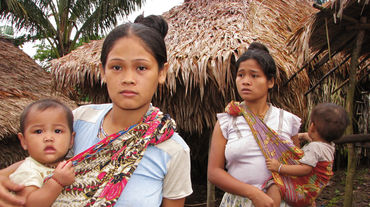 Due donne con i loro figli accanto alle case tradizionali di paglia