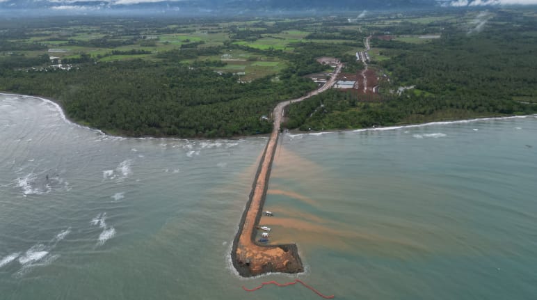 Un pontile marrone conduce dalla miniera di nichel nella foresta pluviale verso il mare. Vista aerea