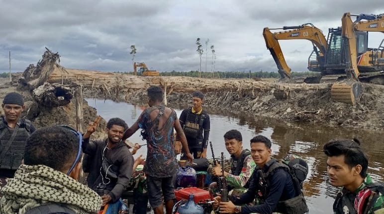 Gruppo di uomini con, sullo sfondo, escavatori meccanici davanti a un paesaggio devastato
