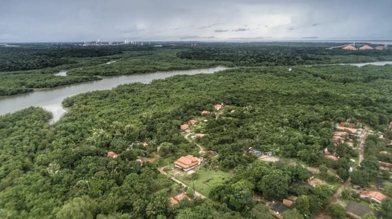 Vista aerea delle case immerse nella rigogliosa vegetazione amazzonica e, sullo sfondo, un fiume con mangrovie sulle rive a Tauá Mirim, Maranhao, Brasile