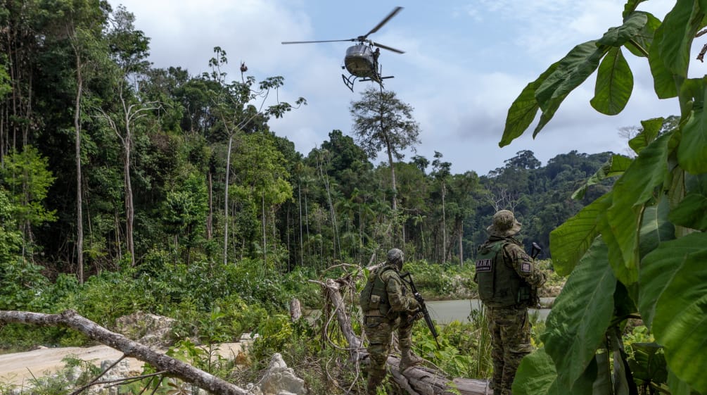 Due agenti armati dell'agenzia ambientale IBAMA, in tuta mimetica, sotto un elicottero durante un'operazione contro l'estrazione illegale di oro nella foresta amazzonica.