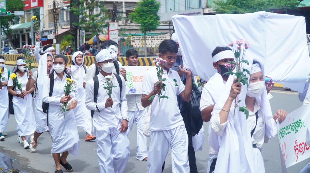 Giovani vestiti di bianco camminano per una strada con fiori in mano a Phnom Penh.