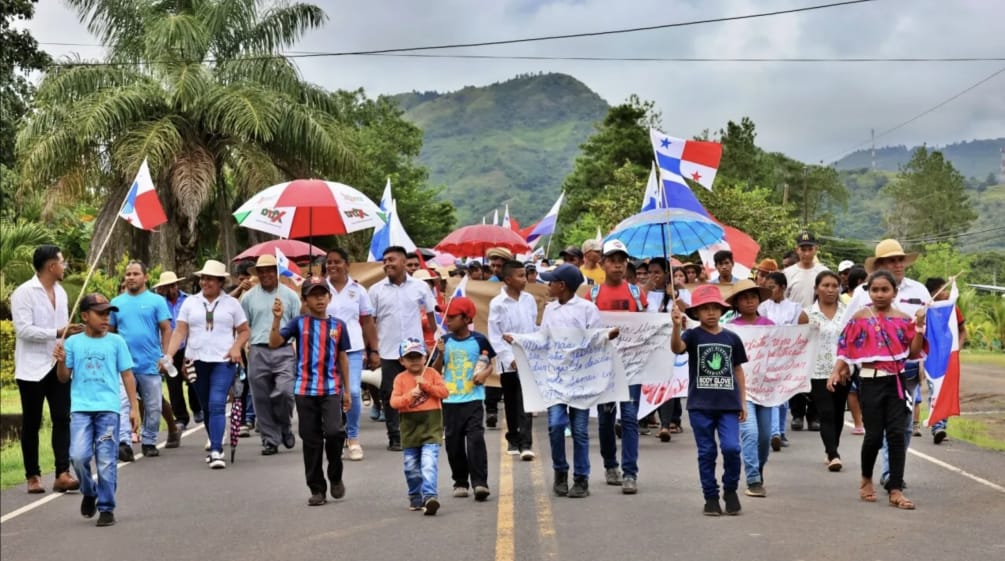 Dimostranti marciano con striscioni, bandiere nazionali e ombrelli lungo un'autostrada a Panama.