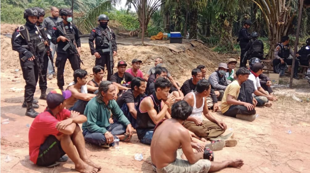 Indigeni Dayak arrestati siedono a terra con la polizia armata alle spalle.